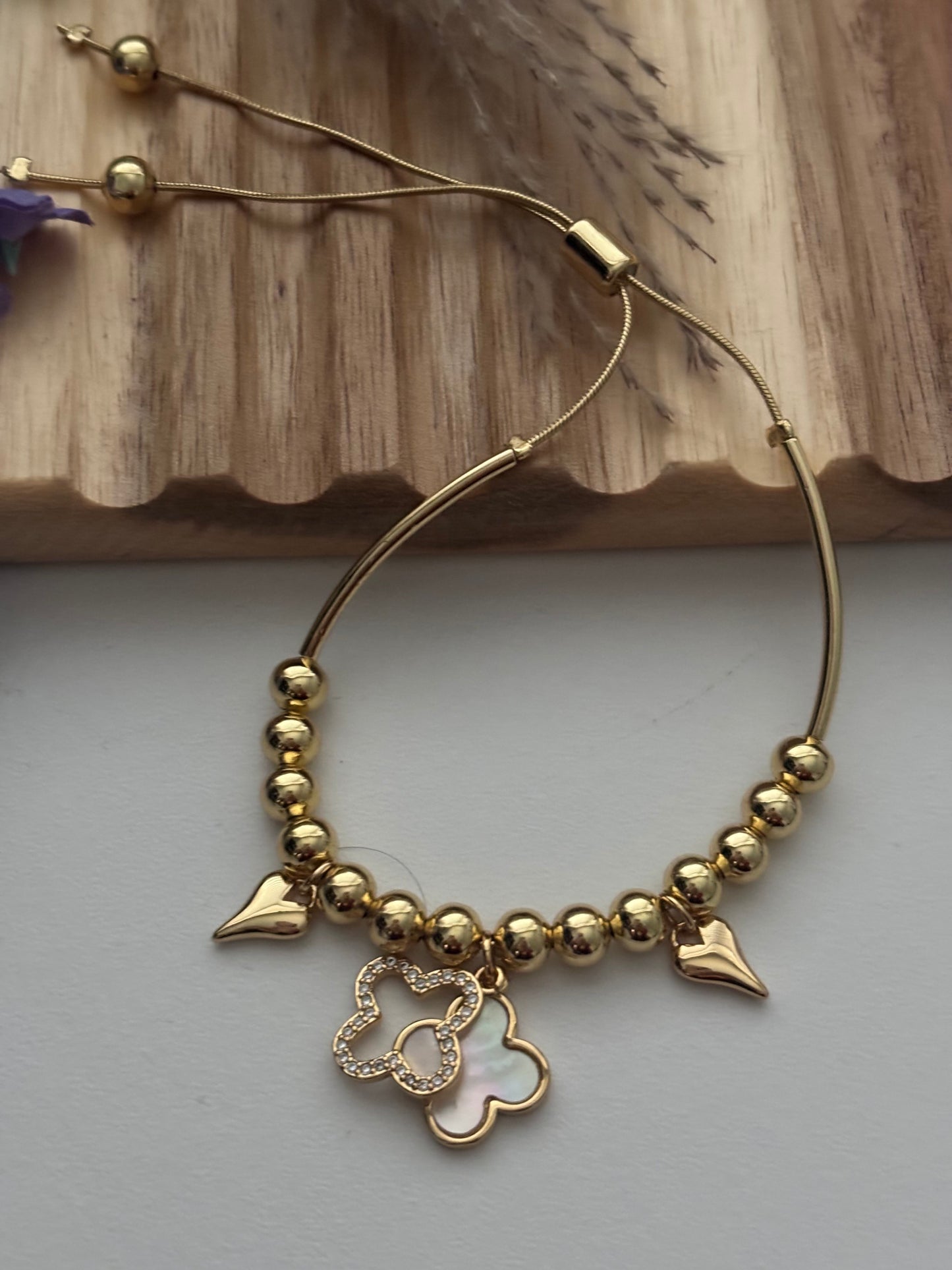 Pulsera dorada con dijes de corazón y trébol