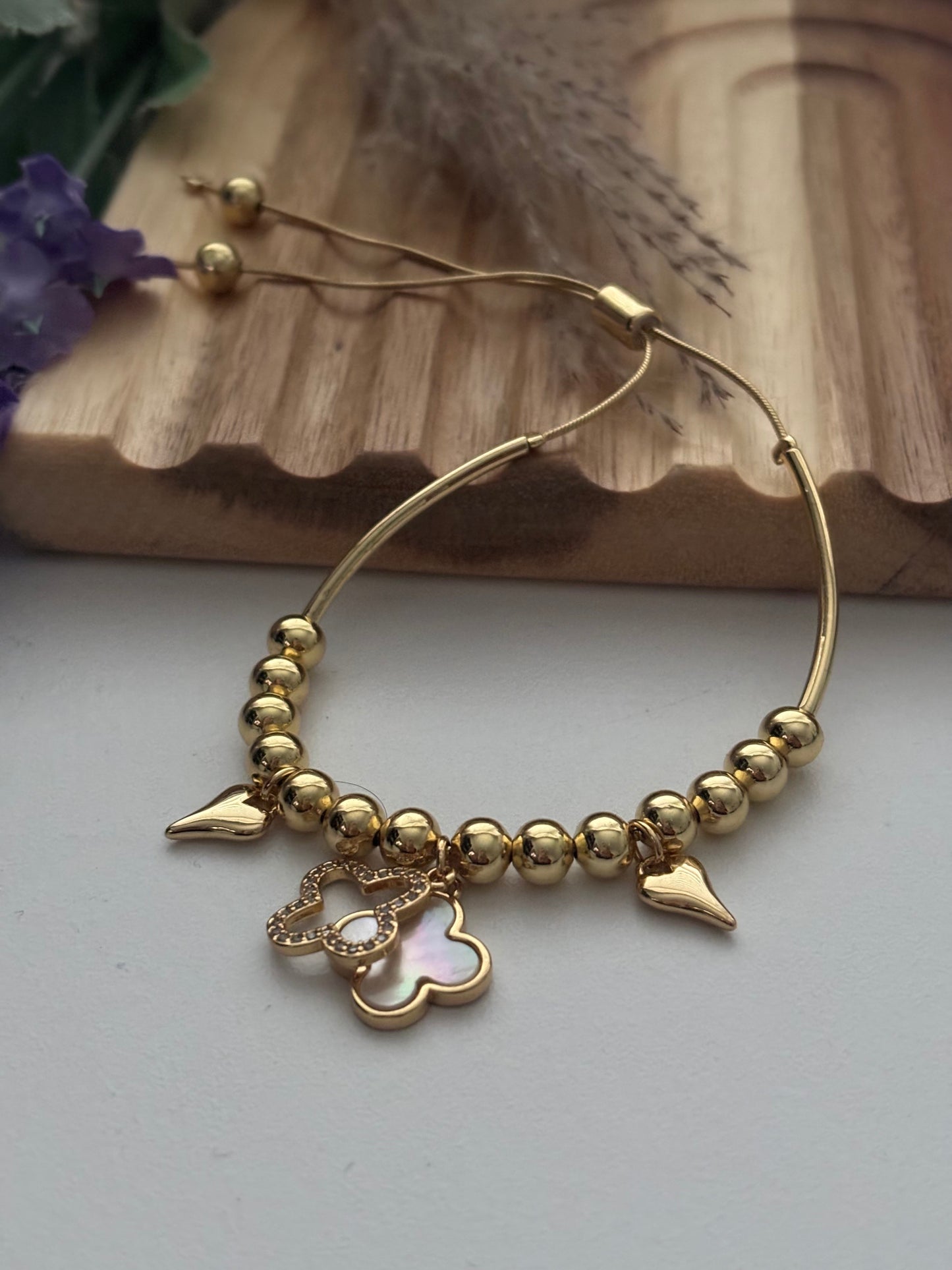 Pulsera dorada con dijes de corazón y trébol